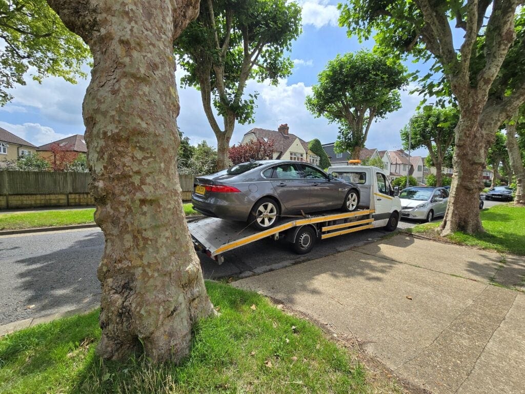 Car recovery London – flatbed tow truck transporting a Jaguar saloon on a residential street.