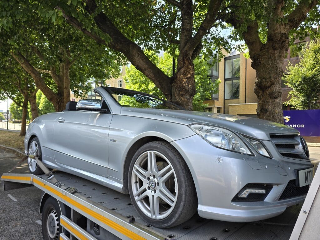 flatbed towing service London transporting a silver Mercedes convertible on a recovery truck in a London street