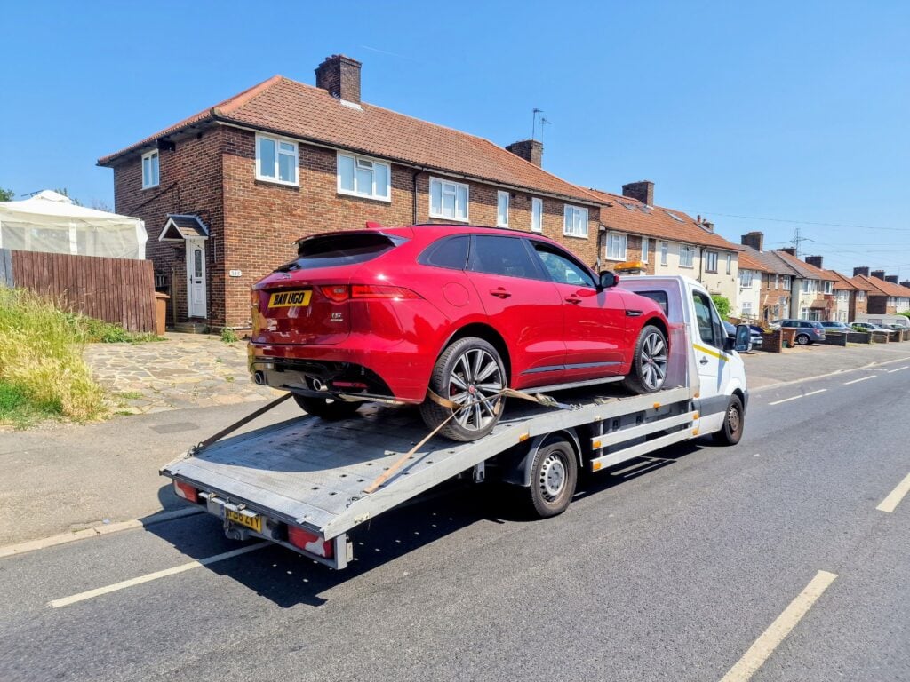 Local towing service London recovering a red Jaguar on a flatbed truck in residential area