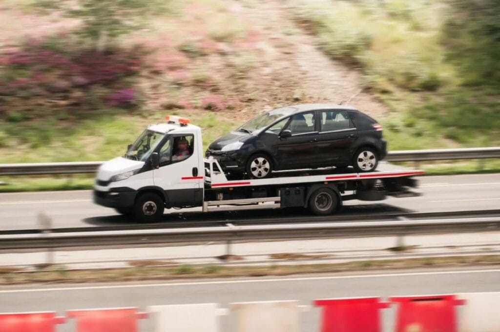 Flatbed tow truck transporting a black hatchback on a UK motorway during breakdown recovery.