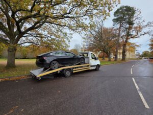 Black Tesla Model 3 being recovered on our flatbed recovery truck in a quiet park-side location during an electric and plug-in hybrid car towing service.