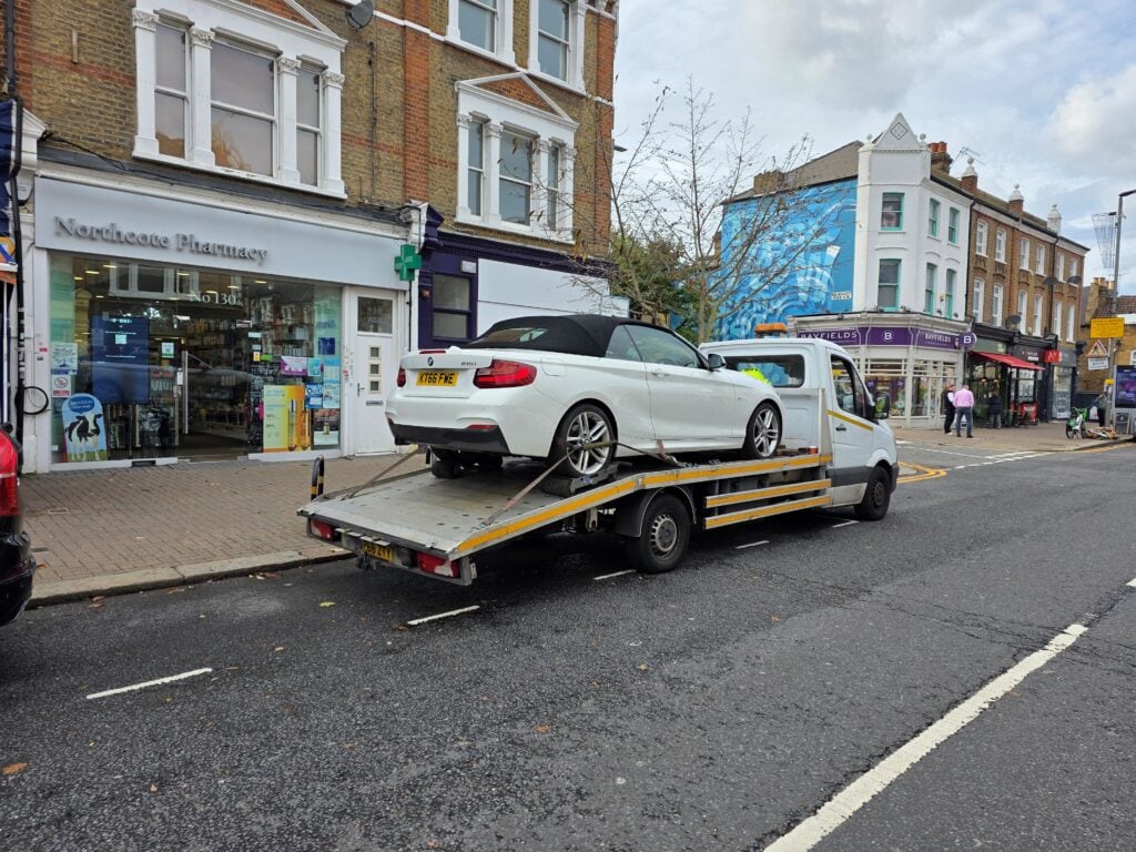 Local flatbed towing service using wheel skates for safe vehicle loading on a London street