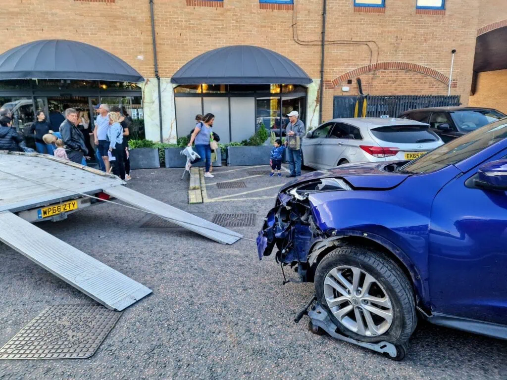 Accident recovery with damaged car on wheel skates being loaded onto a flatbed tow truck in London