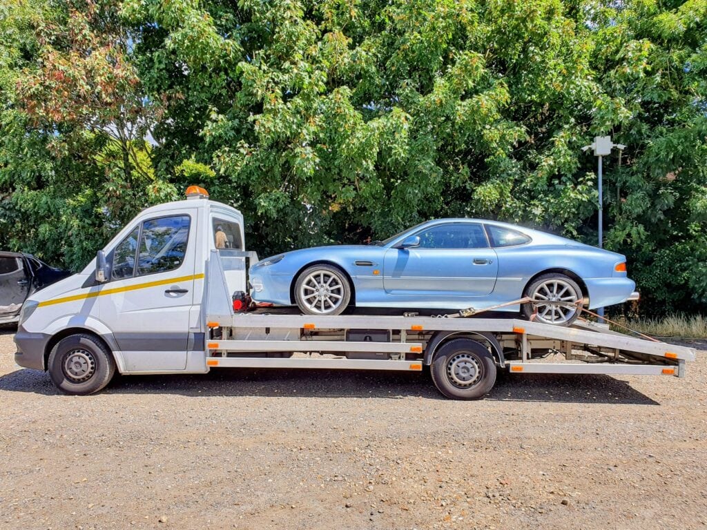 Light blue Aston Martin DB7 loaded onto a flatbed recovery truck, showcasing expert high value car recovery services.