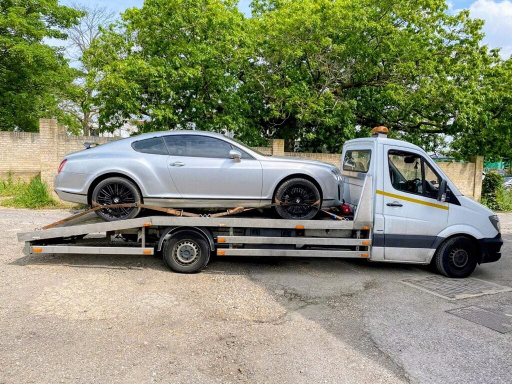 Silver Bentley Continental GT loaded onto a flatbed recovery truck, showcasing white glove luxury vehicle transport.