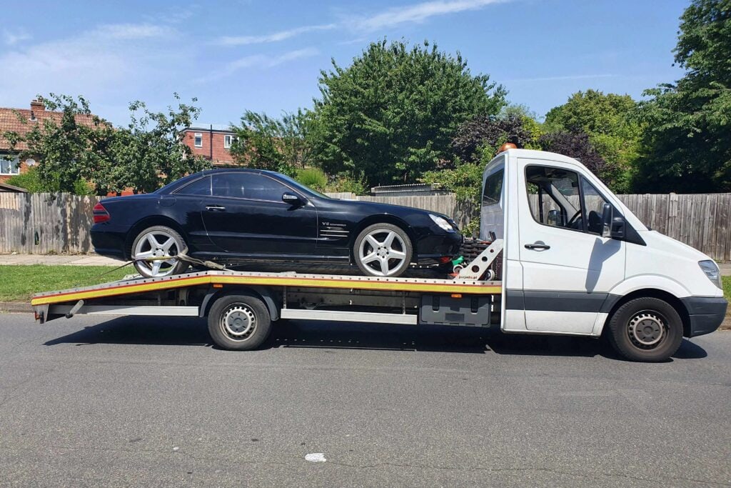 A black Mercedes-Benz SL65 AMG performance roadster being retrieved from a police compound on a flatbed recovery truck in London.