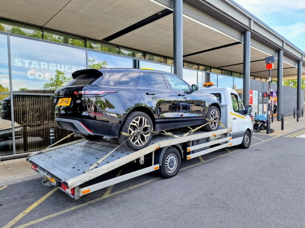A black Range Rover Velar SUV secured on a flatbed recovery truck outside a Starbucks Coffee service station.