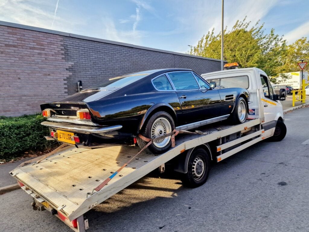 Classic black Aston Martin V8 Vantage loaded onto a flatbed tow truck for high value car recovery service in London, secured with soft straps.