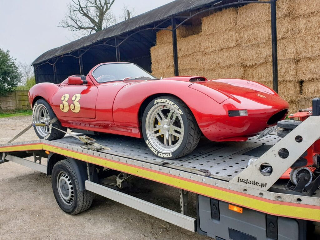 A bright red Gardner Douglas GD T70 Spyder with racing number 33 securely strapped to a flatbed recovery truck, demonstrating specialist classic car transport.