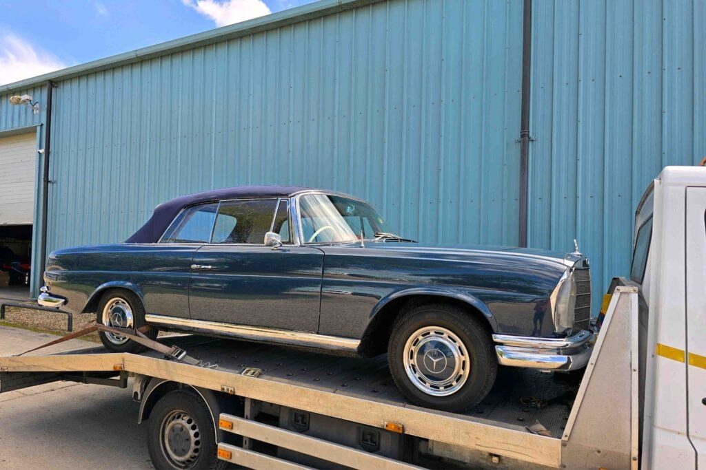 Rear three-quarter view of a classic blue Mercedes-Benz 280 SE convertible securely loaded onto a flatbed recovery truck.