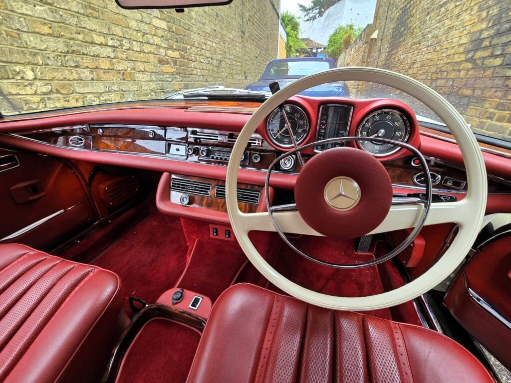 A classic ivory Mercedes-Benz W111 Cabriolet with a red leather interior secured on a flatbed recovery truck in Oxford.