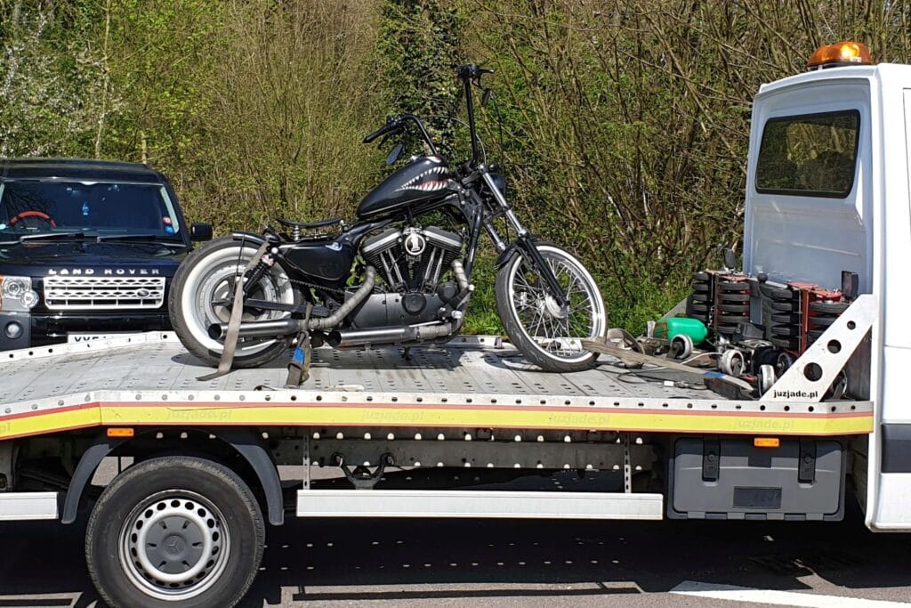 A custom black Harley-Davidson motorcycle with shark mouth tank art and whitewall tires secured on a flatbed recovery truck.