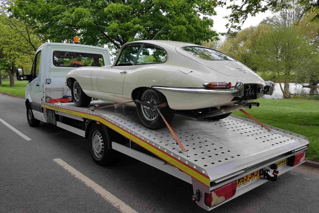 Classic Jaguar E-Type on flatbed recovery truck in London, secured for high value car recovery.