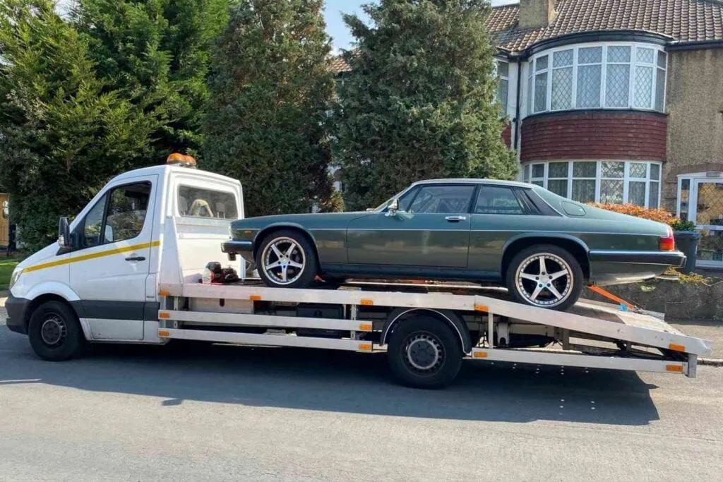 A rare green Jaguar XJ Coupé securely loaded onto a flatbed truck, showcasing our professional towing company services in London.