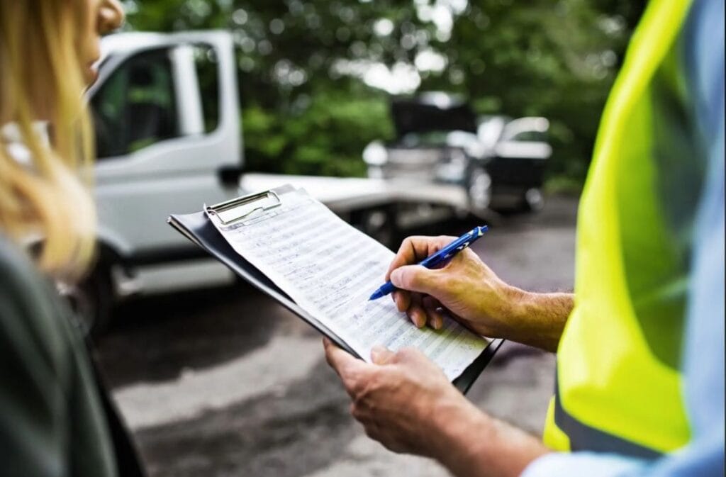 London Auto Towing operator completing recovery documentation on a clipboard beside a flatbed tow truck.
