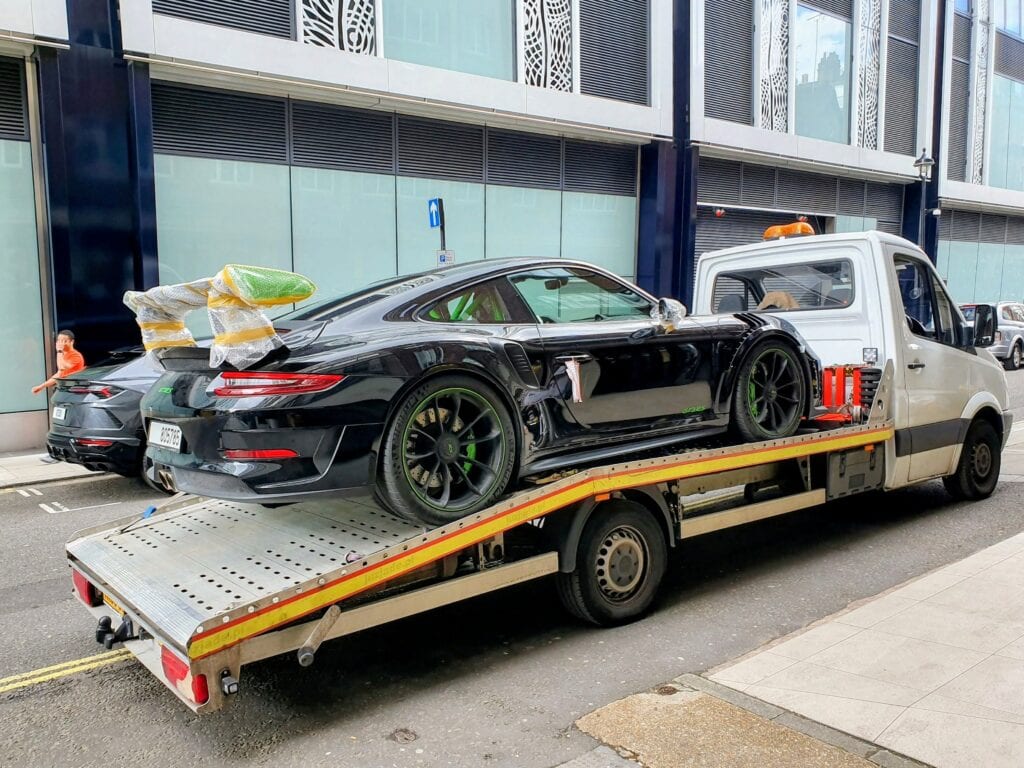 Black Porsche 911 GT3 RS with protective transport wrapping loaded onto recovery truck after collection from shipping company.