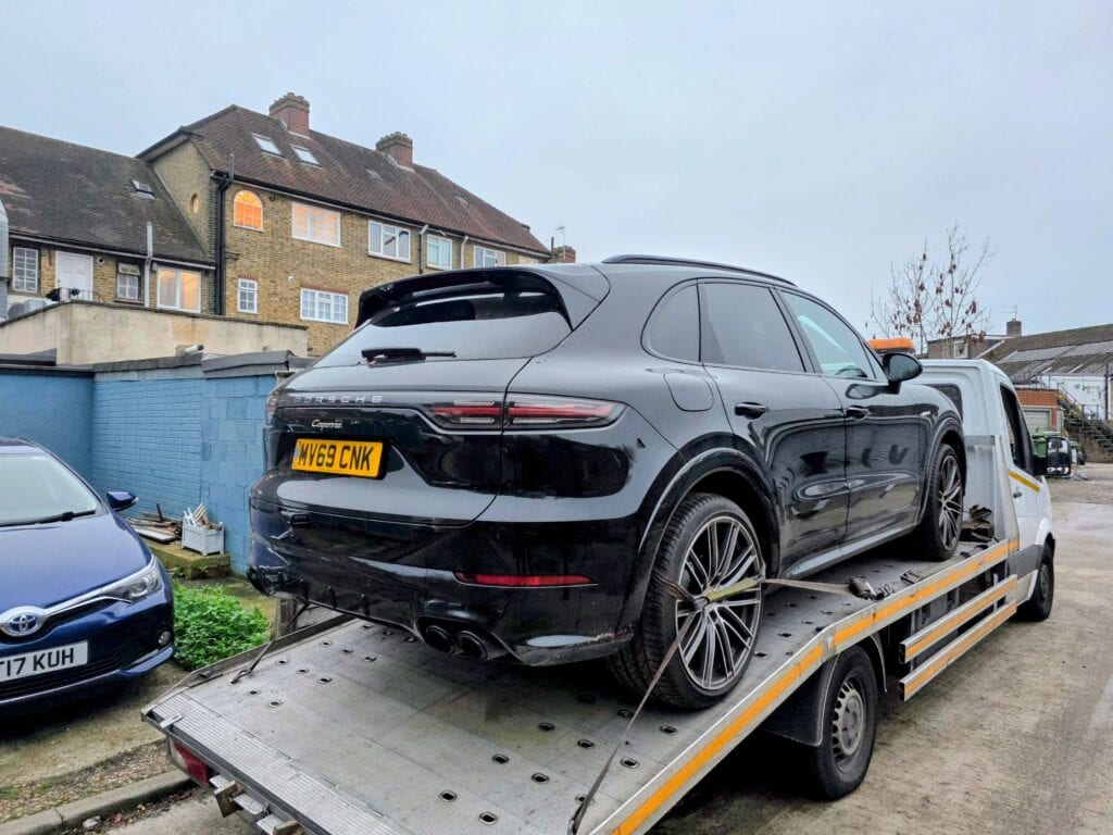 Black Porsche Cayenne loaded onto recovery truck in a London residential area due to starter motor failure.