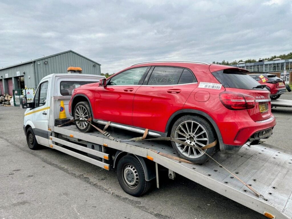 A red Mercedes-Benz GLA being transported on a flatbed recovery truck from a York auction to London.