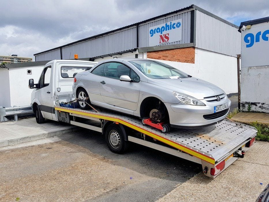Scrap car collection of a damaged Peugeot loaded on our flatbed tow truck