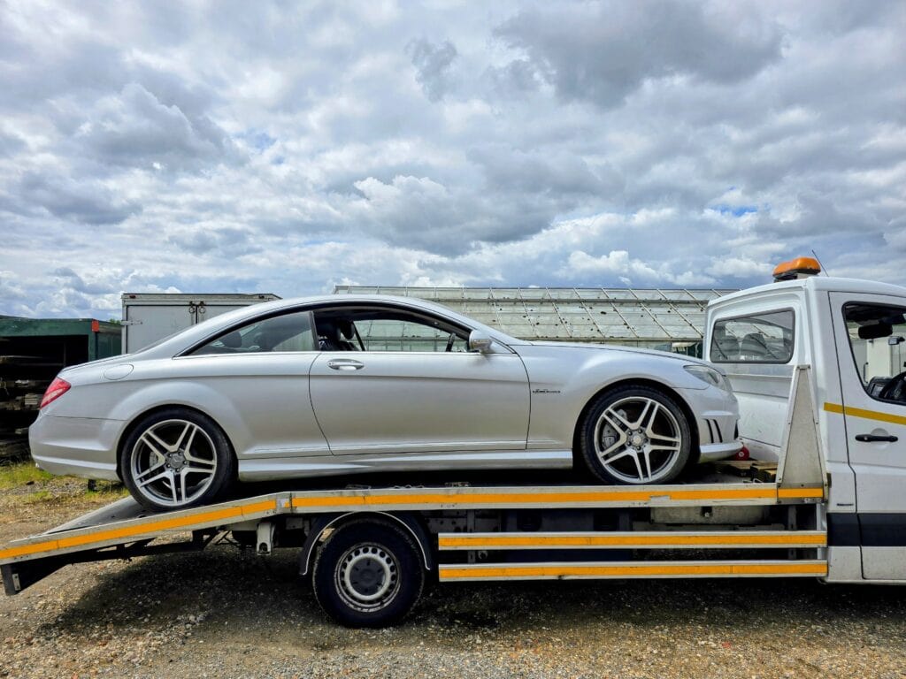 A silver Mercedes CL63 AMG performance coupe being transported on a professional flatbed recovery truck in a local Surrey yard.