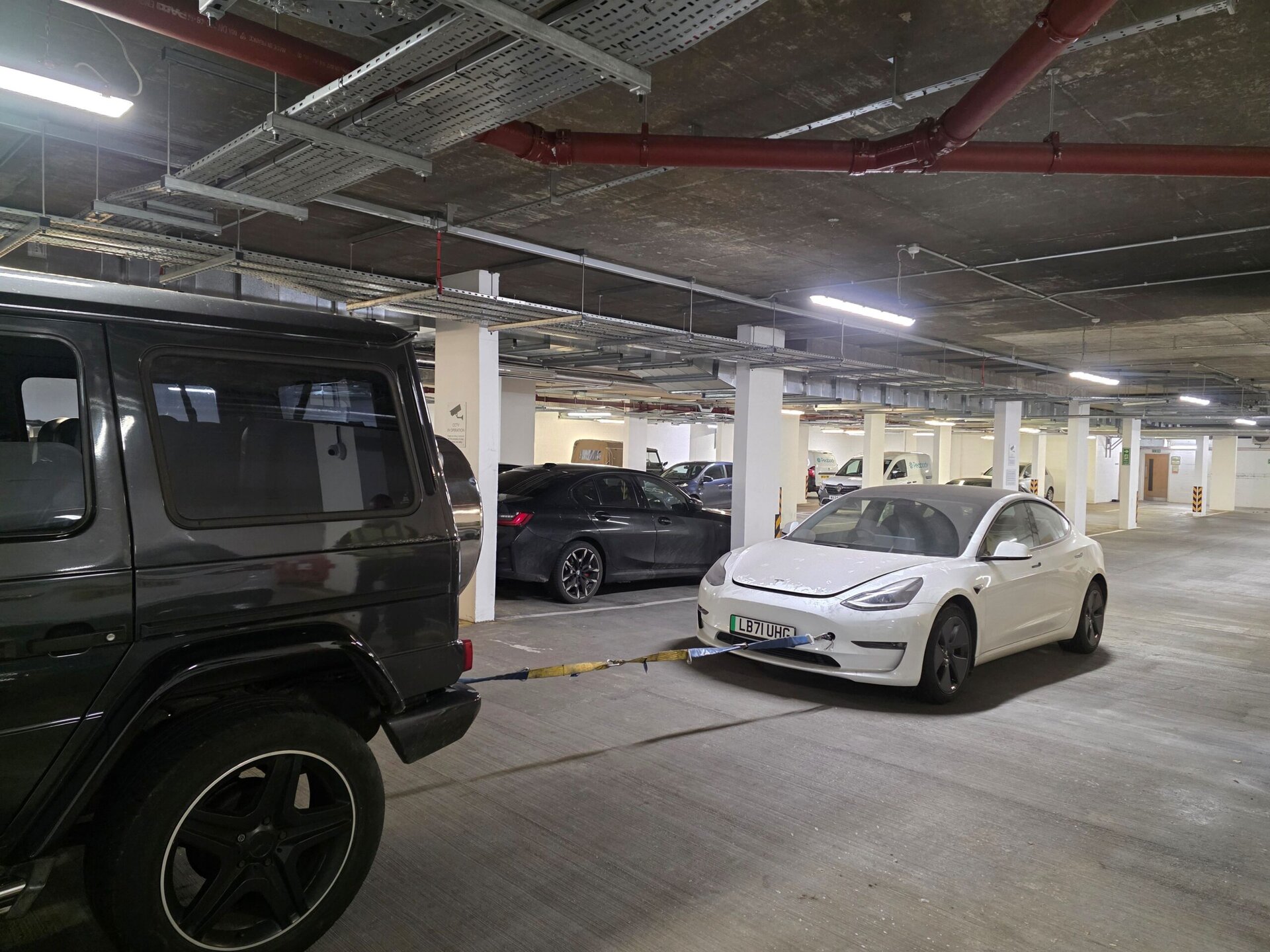 Tesla Model 3 being carefully moved out of an underground car park using a controlled tow to reach open space for recovery.