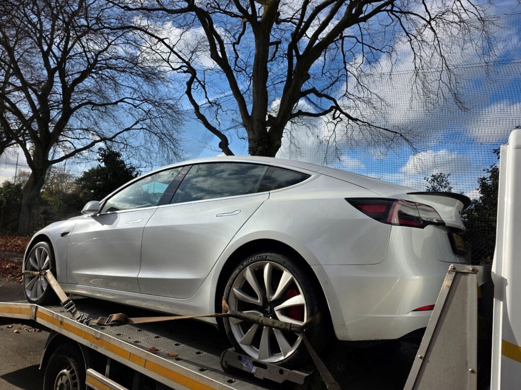 Tesla Model 3 electric vehicle loaded onto a flatbed recovery truck using wheel skates after tow mode issues in London.