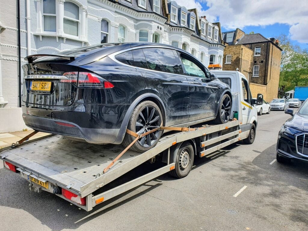 Black Tesla Model X loaded onto a flatbed recovery truck in London after a system update freeze.