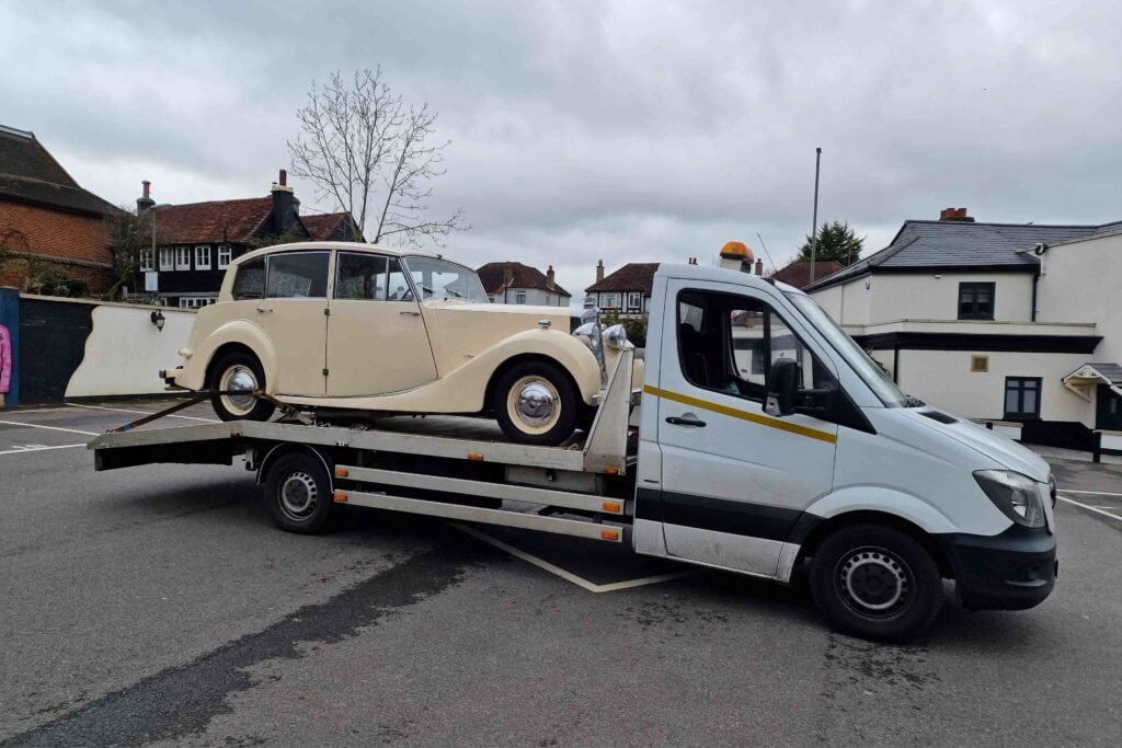 A cream vintage Triumph Renown wedding car securely loaded onto a flatbed recovery truck, demonstrating specialist breakdown support for events.