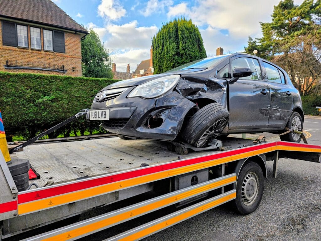 Vauxhall Corsa accident recovery with damaged front suspension loaded on wheel skates onto a flatbed tow truck
