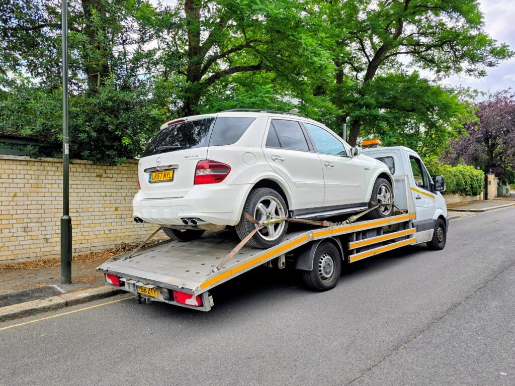 A white Mercedes-Benz ML63 AMG performance SUV being loaded onto a flatbed recovery truck for emergency breakdown recovery in London.