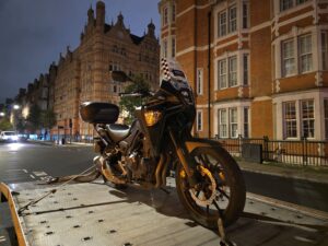 Professional emergency motorbike recovery Richmond service securing a black adventure motorcycle onto a flatbed tow truck at night.