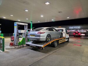 Professional local roadside assistance Richmond service recovering a silver Porsche Panamera onto a flatbed tow truck at a BP petrol station.