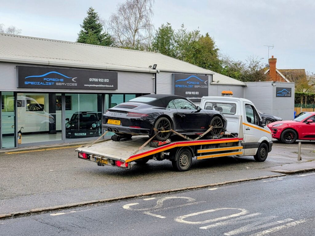 White flatbed tow truck safely transporting a black Porsche for professional high value car recovery and reliable breakdown recovery near me.