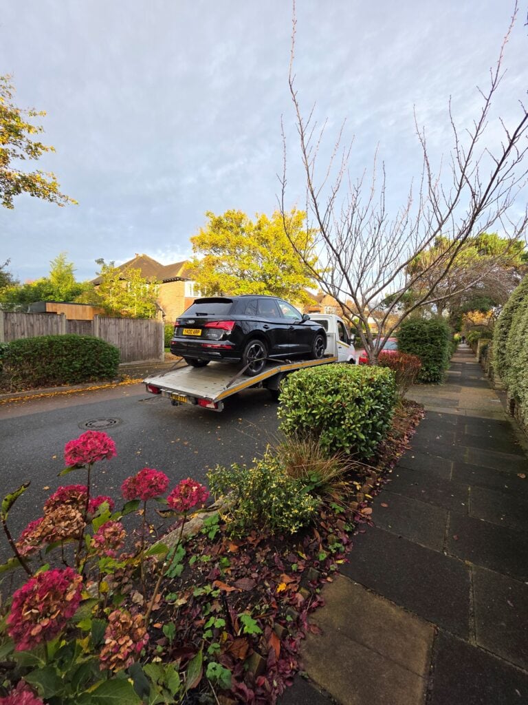 Black Audi Q5 hybrid being safely loaded onto a London Auto Towing flatbed recovery truck in a residential Kingston street.