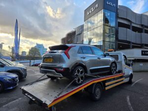 Electric car recovery Twickenham featuring a silver Kia EV6 secured on a flatbed recovery truck outside a Kia dealership.