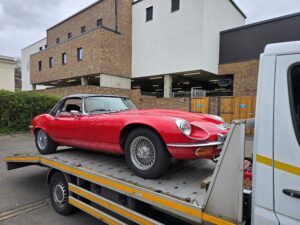 Classic red Jaguar E-Type being transported via a professional towing service in Twickenham on a modern flatbed recovery truck.