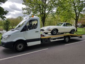 High value classic car recovery Twickenham featuring a pristine white Jaguar E-Type Coupe secured on a white flatbed recovery truck.