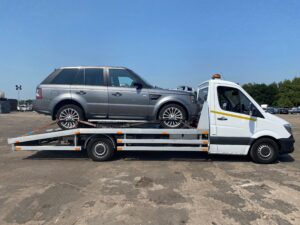 Professional impound car recovery of a grey Range Rover Sport on a white flatbed tow truck from a London police compound for breakdown recovery services.