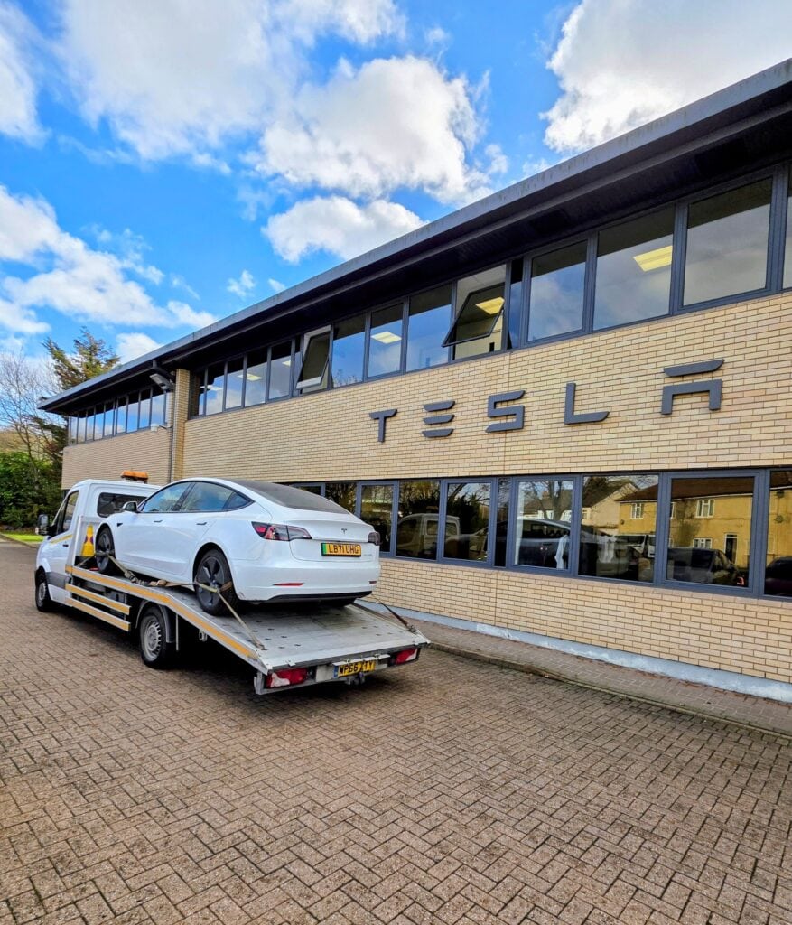 Electric car recovery Kingston white Tesla secured on flatbed tow truck outside Tesla centre.