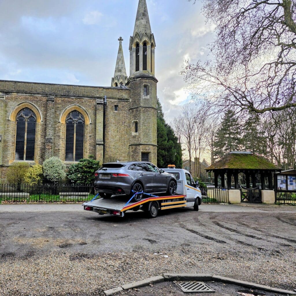 A professional outdoor photo of a gray Jaguar F-PACE securely loaded on a modern flatbed recovery truck.