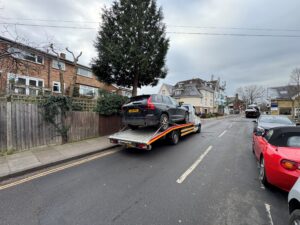 Professional collection of a black Volvo XC60 SUV using a flatbed recovery truck for our we buy any cars service in Twickenham.