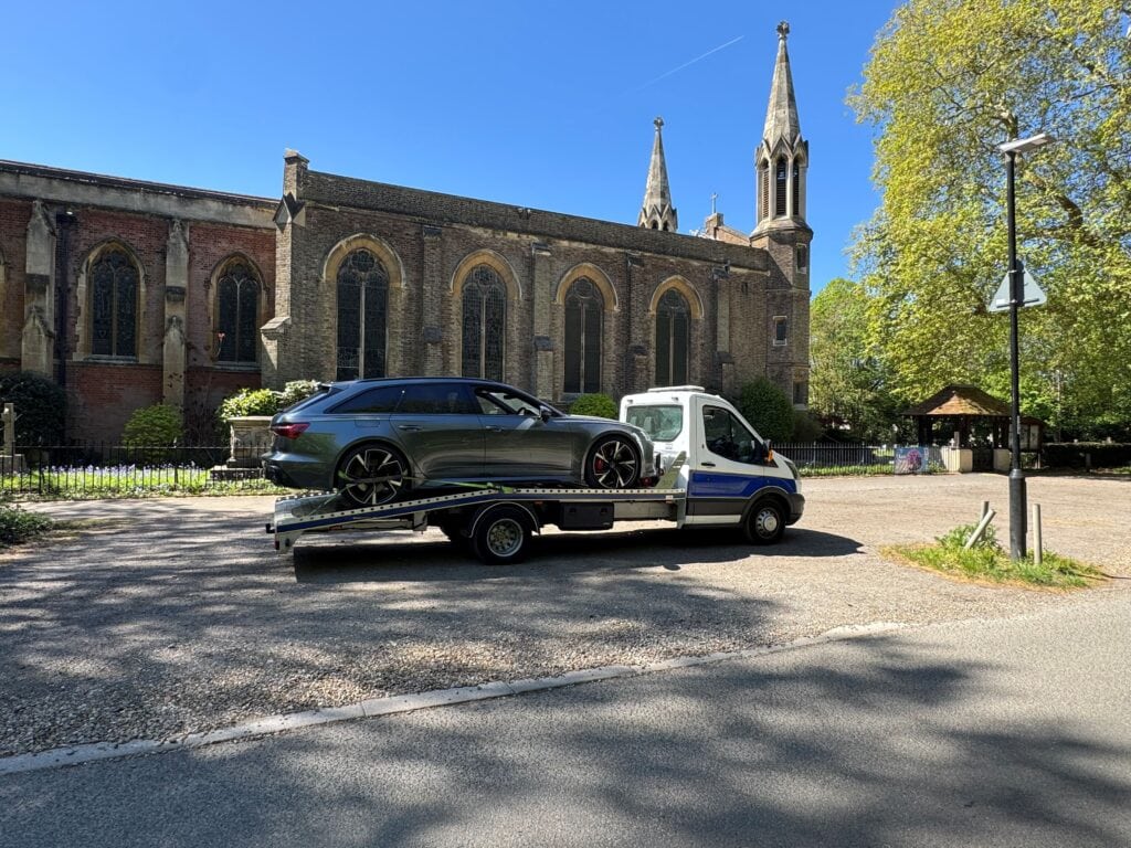 Audi RS6 performance car recovery on a professional flatbed towing service truck in Fulham outside a historic local church.
