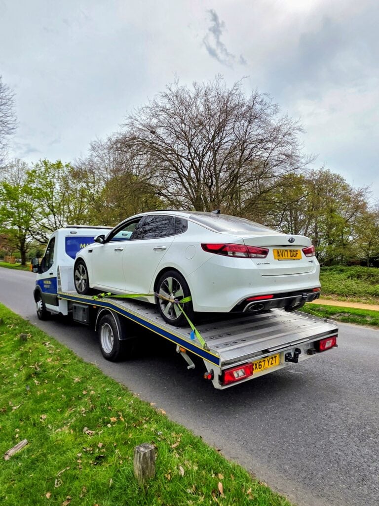 White Kia Optima on a flatbed tow truck for local breakdown recovery Wimbledon near Royal Wimbledon Golf Club in the SW19 area.