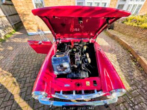 Red classic MG Midget receiving a professional car battery jump start service in Fulham on a residential driveway in SW6 area.