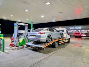 Silver Porsche Panamera on a flatbed tow truck for emergency car recovery Fulham at a petrol station during the night in SW6.