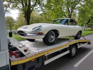 White Jaguar E-Type on a flatbed tow truck for luxury car recovery Fulham near a local park in the SW6 area of London.