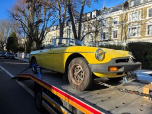 Yellow MGB Roadster on a flatbed tow truck for expert roadside assistance and classic car recovery in Kensington London area.