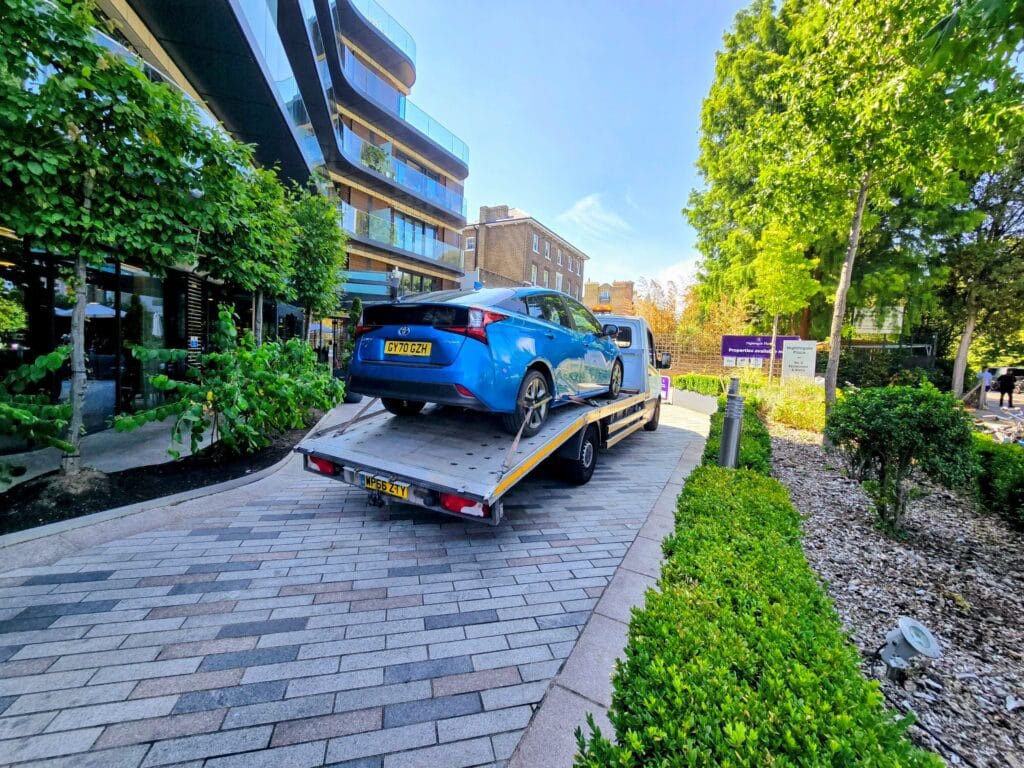Blue Toyota Prius Hybrid being delivered by flatbed recovery truck for a car recovery Wimbledon customer following expert scrap car collection.