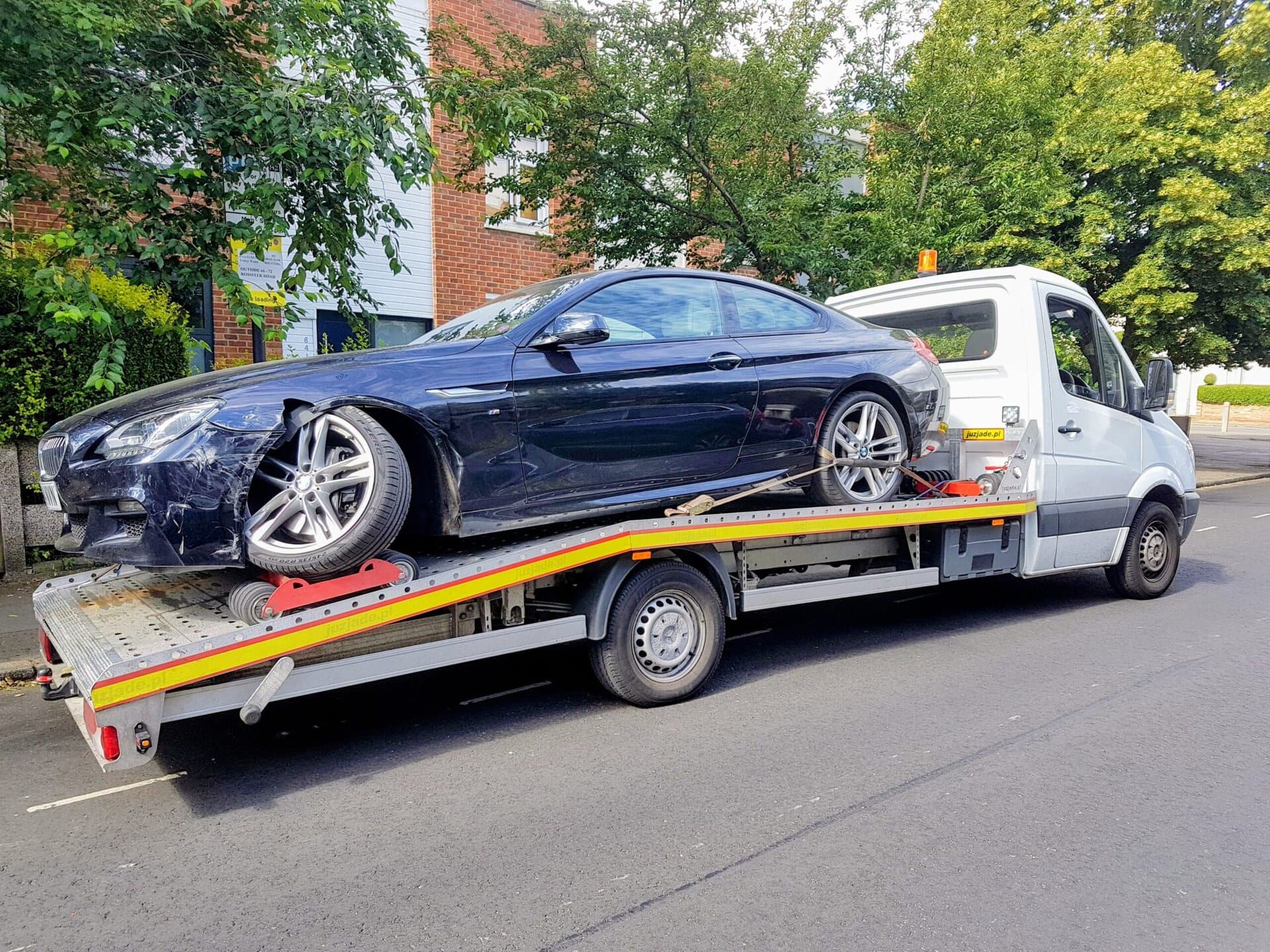 Specialized accident recovery: Dark blue BMW on a flatbed. Red skate supports a damaged front wheel for safe transport.