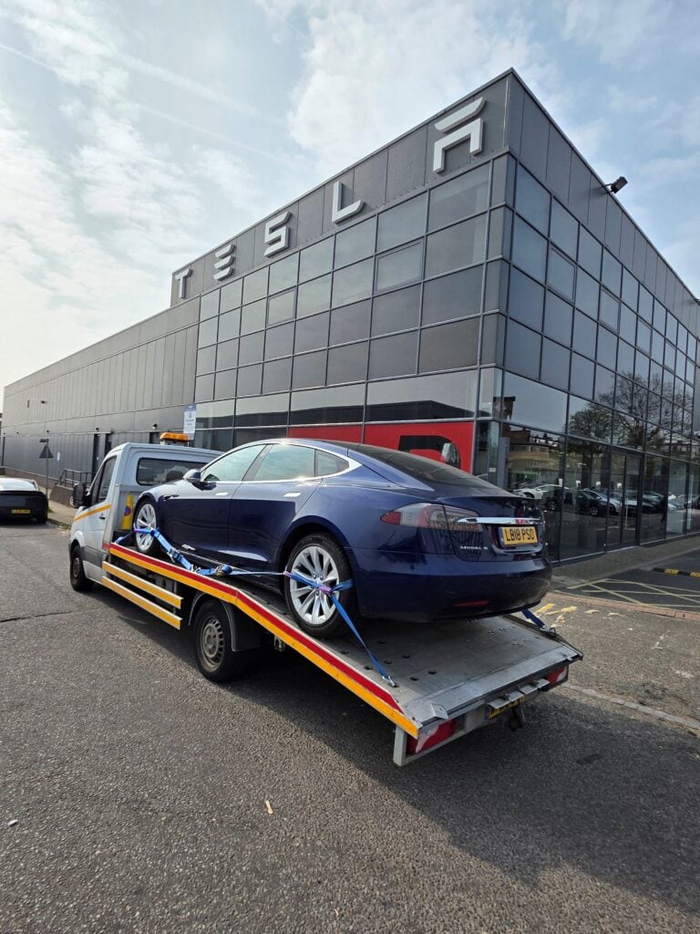 Tesla Model S securely loaded on flatbed recovery truck outside Tesla dealership — electric car recovery and towing service West London